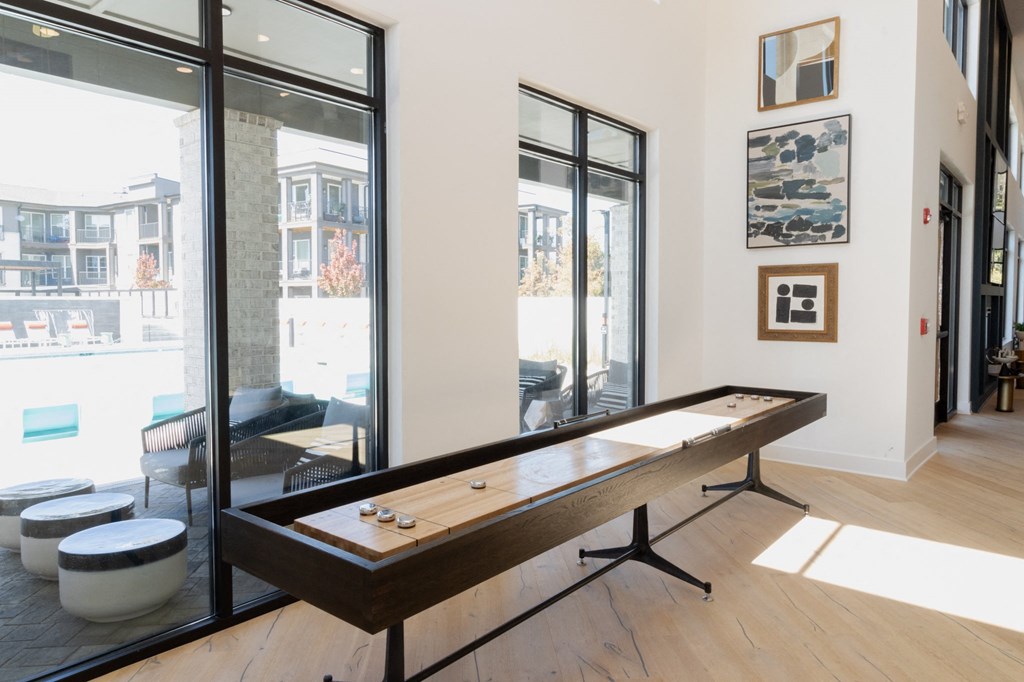 a shuffleboard table in a room with large windows at The Wren Apartments, Lawrenceville, GA
