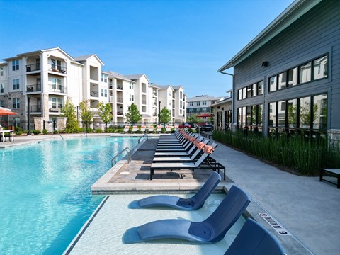 A swimming pool with lounge chairs and apartment buildings in the background.