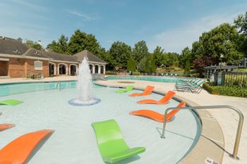 a swimming pool with a fountain and orange and green chairs at The Crest at Sugarloaf, Lawrenceville, GA, 30044