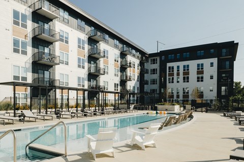 a swimming pool with lounge chairs in front of an apartment building