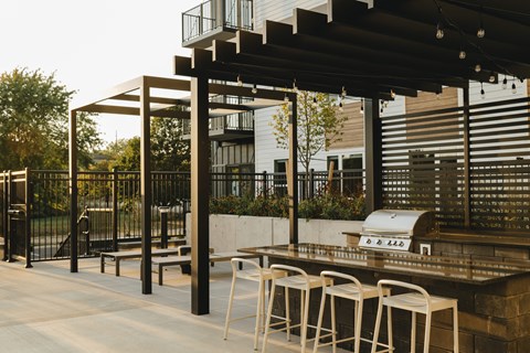 a patio with a barbecue grill and chairs under a roof