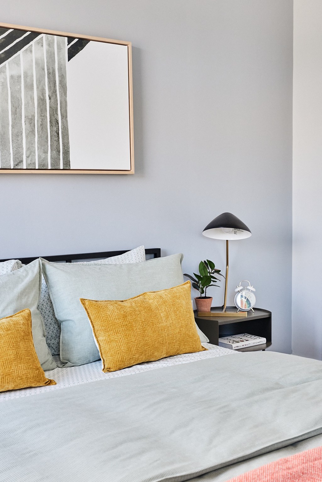 a bed with pillows and a nightstand with a lamp and a picture above