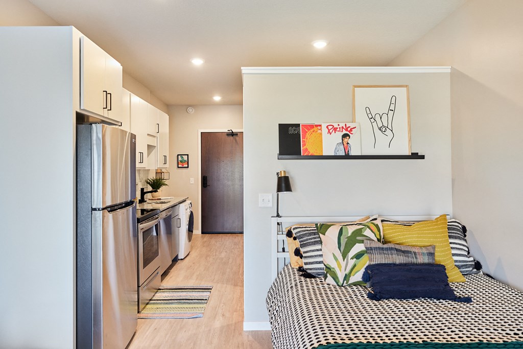 a bedroom with a bed and a refrigerator in a room with a kitchen