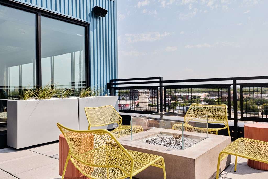 a seating area with yellow chairs and a fire pit on a balcony