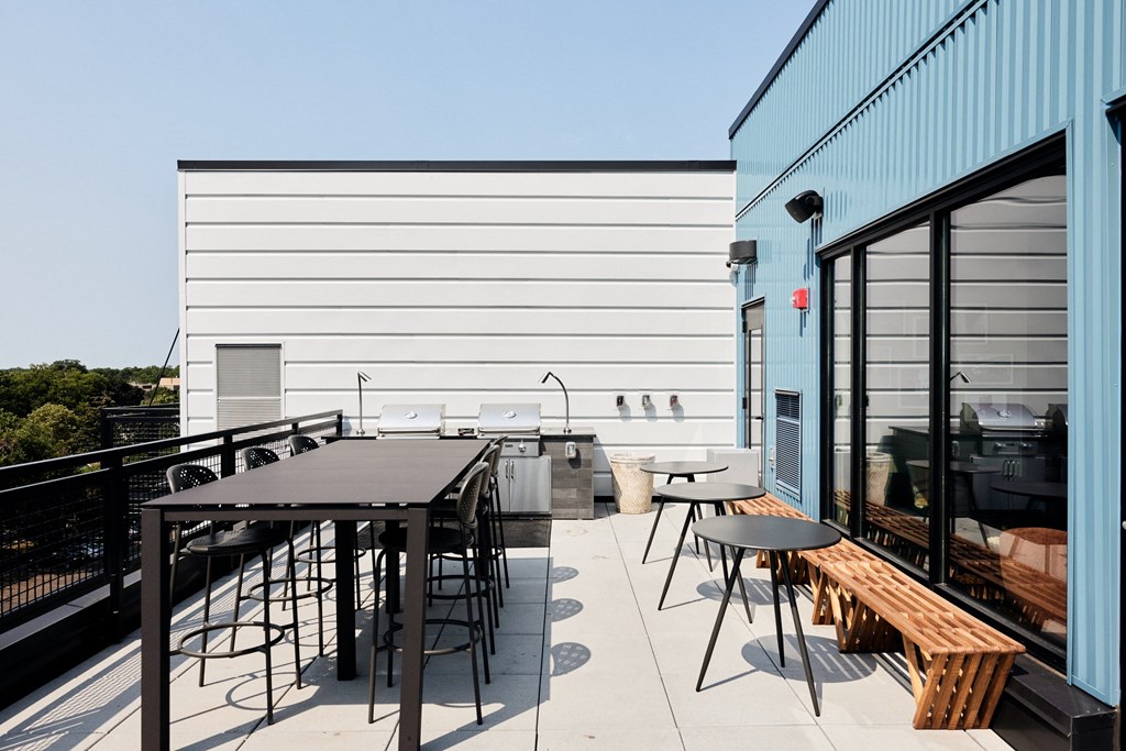 a rooftop patio with tables and chairs and a barbecue grill