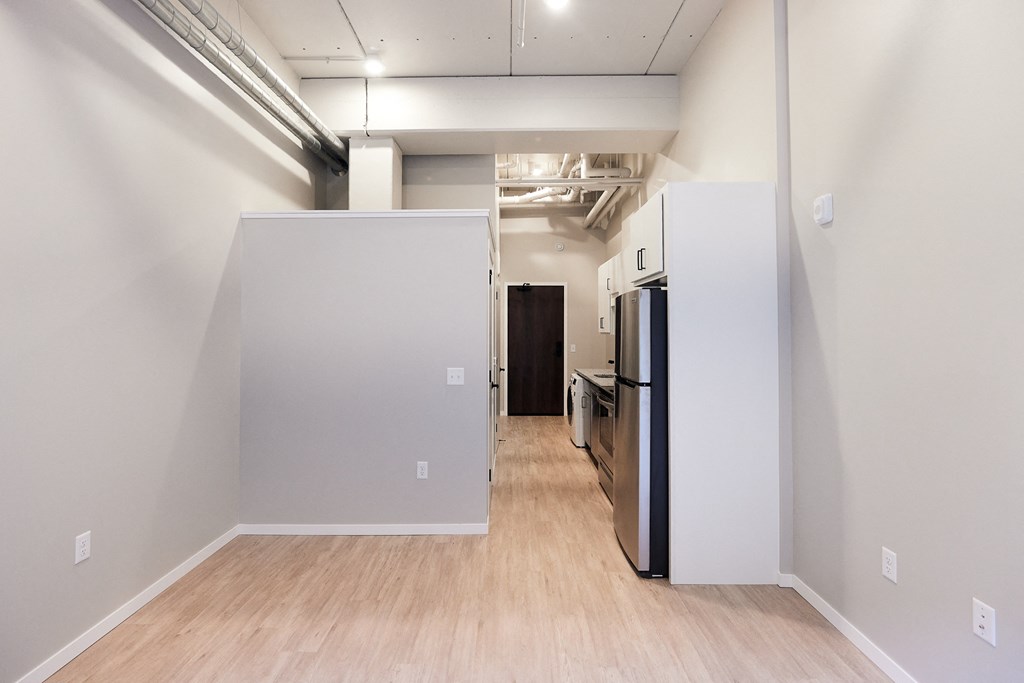 an empty room with white walls and a wood floor and a kitchen