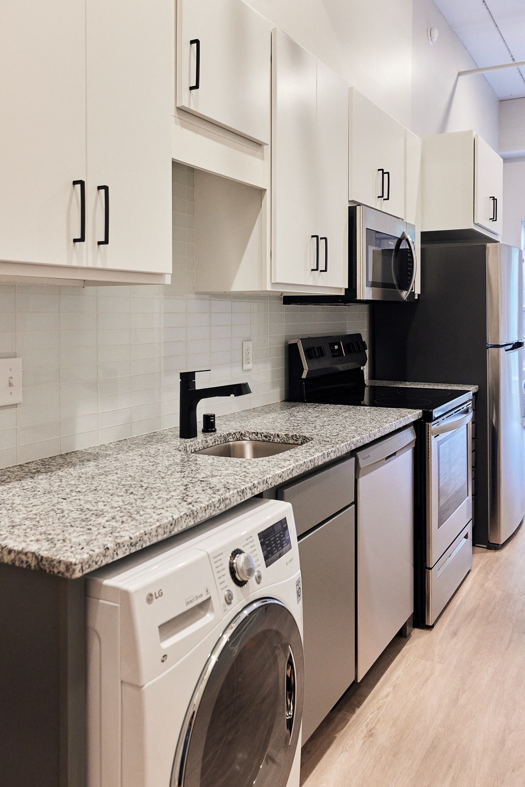 a washer and dryer in a kitchen with white cabinets and a granite counter
