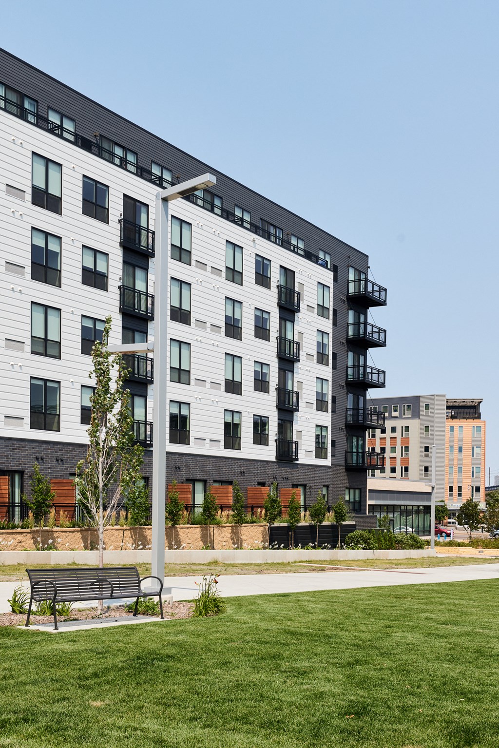 a large white apartment building with a green lawn and a bench