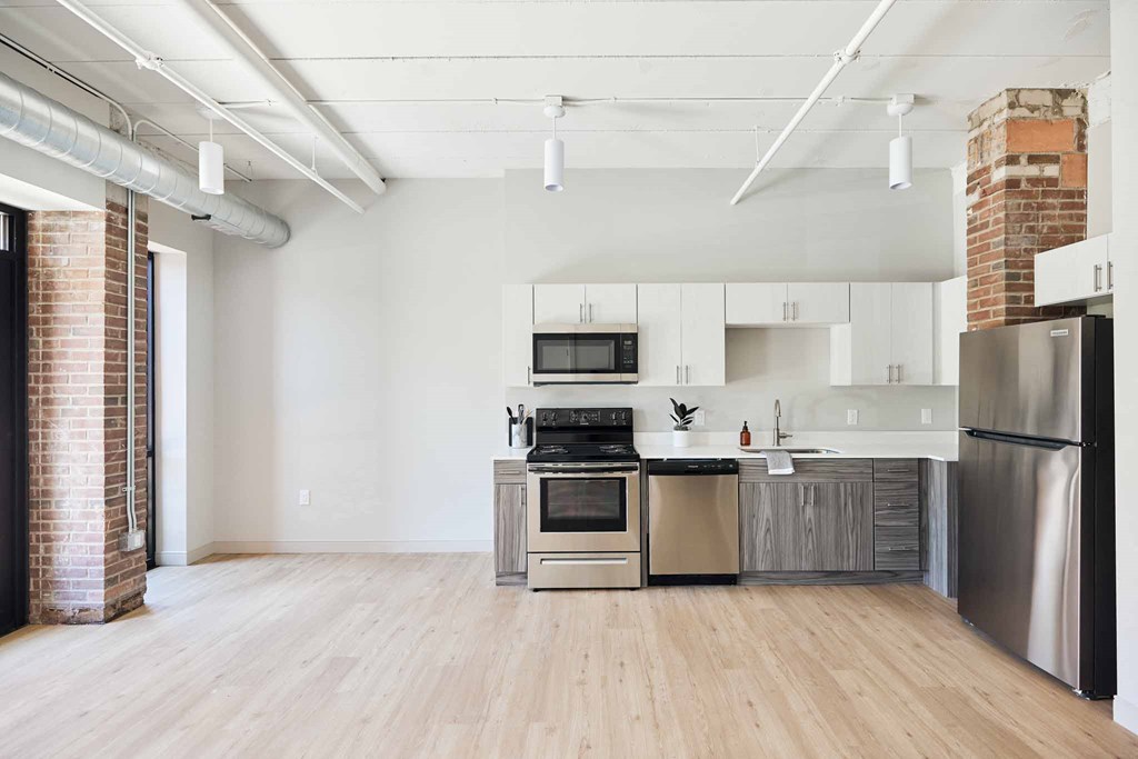 an empty living room with a kitchen with stainless steel appliances