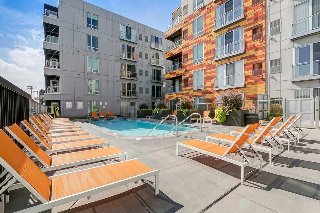 a pool with lounge chairs in front of an apartment building