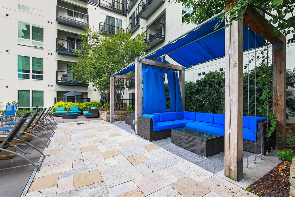 an outdoor patio with blue couches and chairs in front of an apartment building