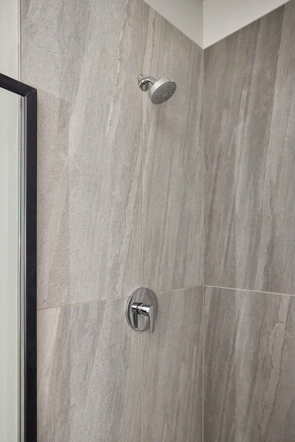 a grey tiled shower in a bathroom with a glass door
