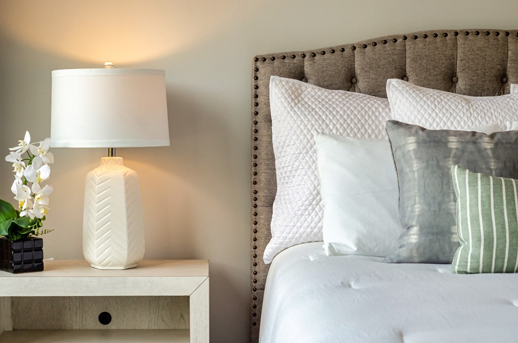 a bed with pillows and a white lamp on a night stand