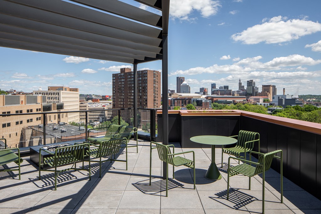 a balcony with green chairs and tables and a city in the background