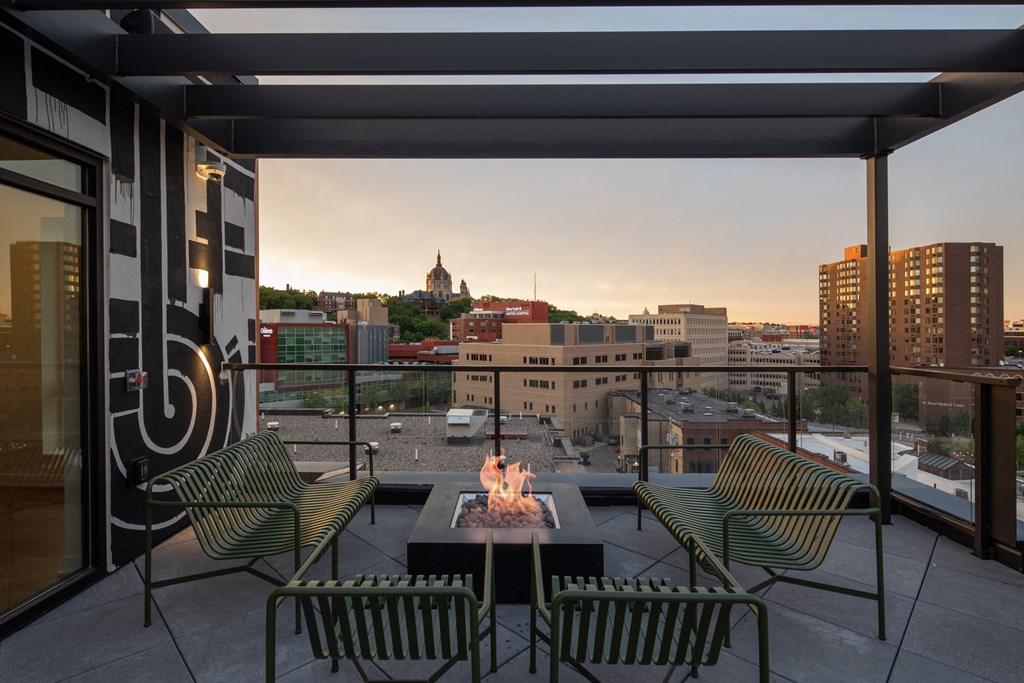 a balcony with a fire pit and chairs and a city in the background