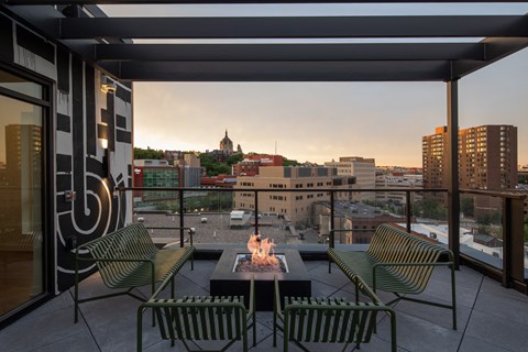 a balcony with a fire pit and chairs and a city in the background
