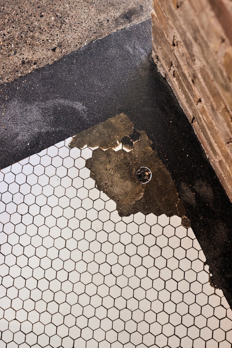 a bathroom with black and white tile and a damaged floor
