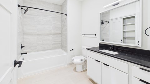 A white bathroom with a black counter top and a toilet in the corner.