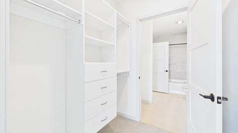 A white closet with drawers and shelves is open to a hallway.