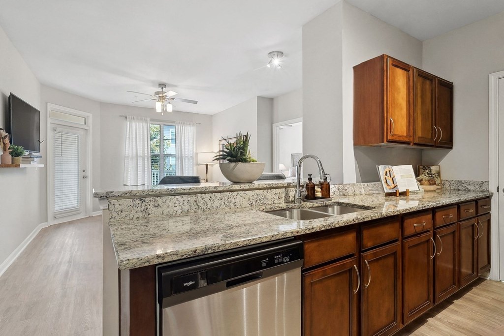 luxury kitchen with granite countertops open to a spacious living room with a ceiling fan at Sorelle apartments