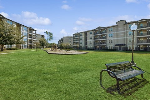 greenspace area with a park bench and playground area at Park at Magnolia apartments