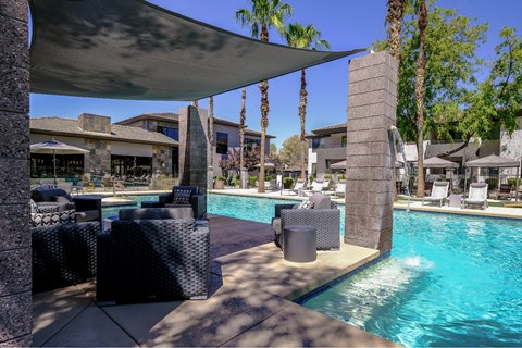 A pool area with a stone pillar and a shade structure.