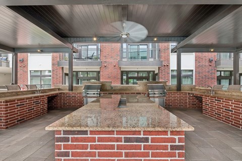A large outdoor kitchen area with a brick countertop and a ceiling fan.