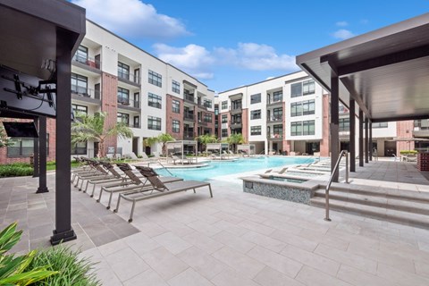 A pool area with sun loungers and a building in the background.