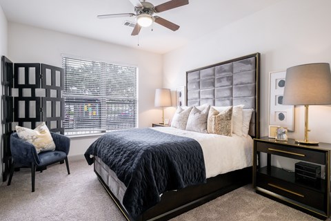 A bedroom with a bed, chair, and a ceiling fan.