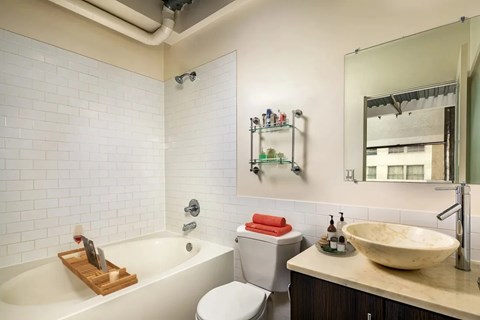 A white tiled bathroom with a wooden tray in the tub.