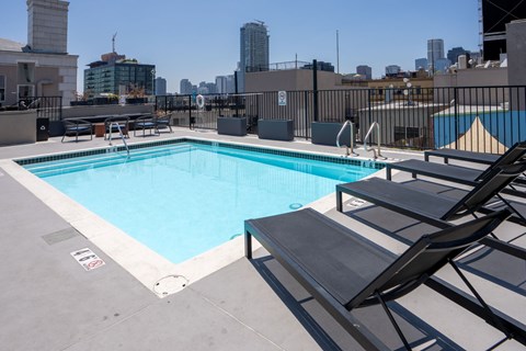 A swimming pool on a rooftop with lounge chairs and a city skyline in the background.