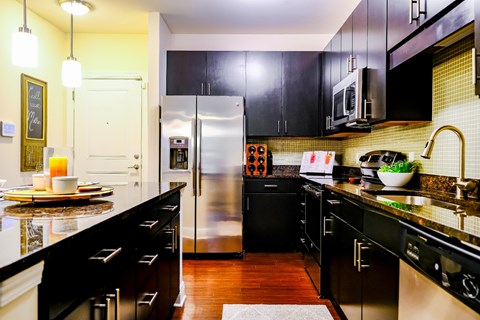 A kitchen with black cabinets and a stainless steel refrigerator.