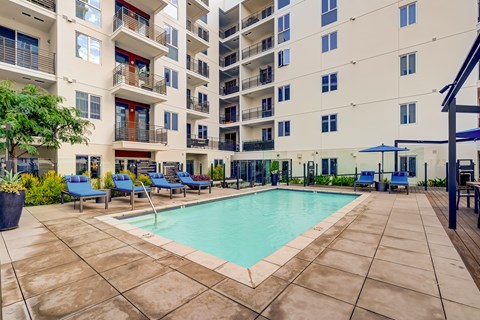 A large swimming pool surrounded by a tiled patio and lounge chairs.