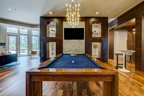A pool table in the middle of a room with a TV and a chandelier.