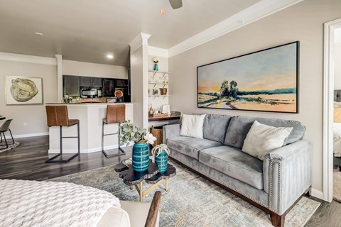A living room with a grey couch and a painting on the wall.