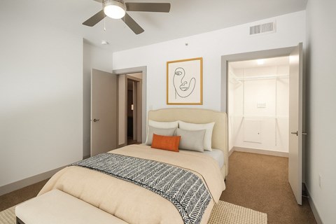 A bedroom with a bed, a ceiling fan, and a painting on the wall.