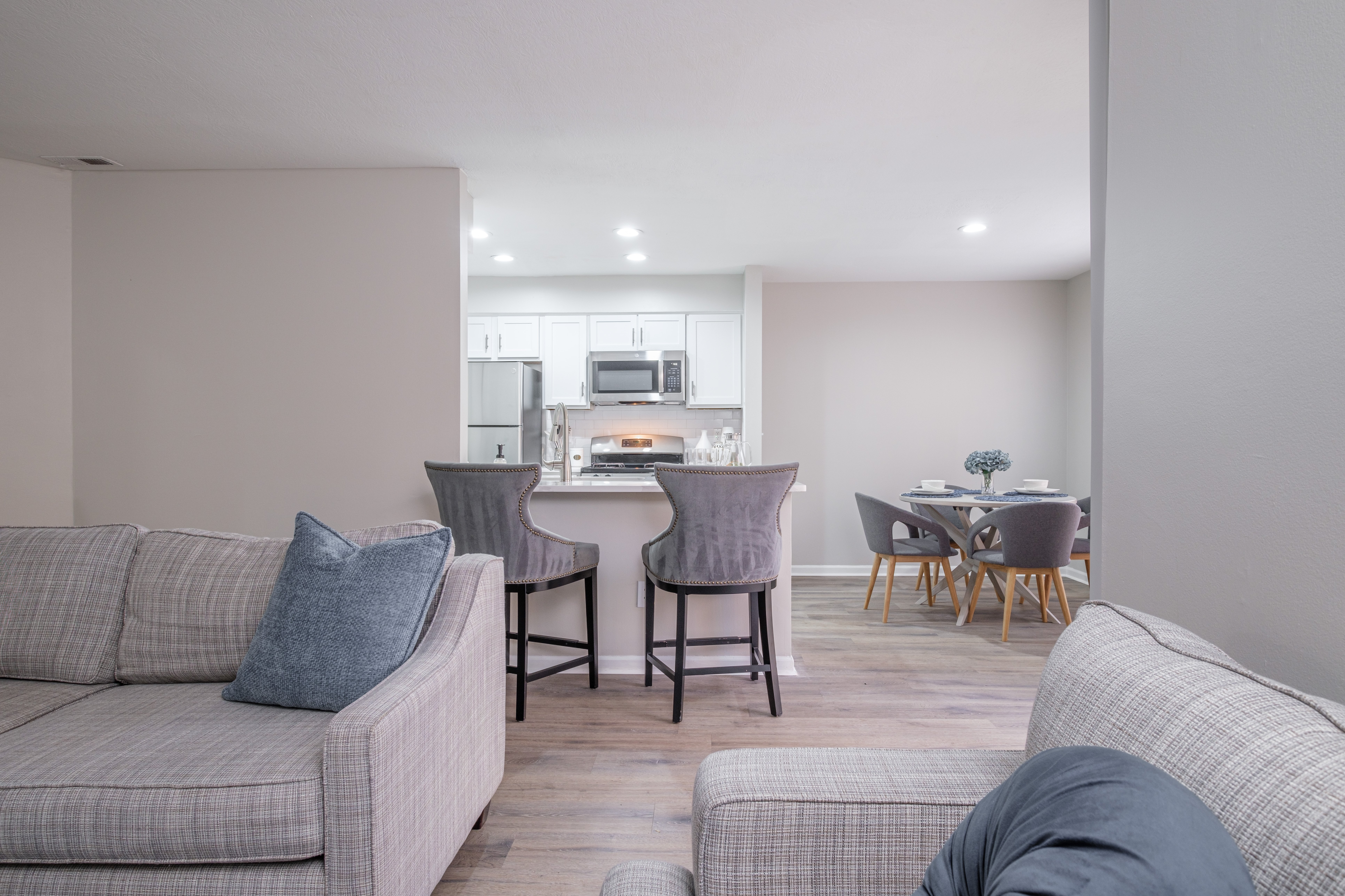 A living room with a grey couch and a dining table with chairs.