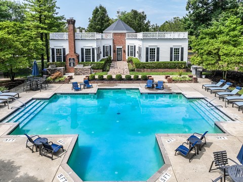 A large swimming pool surrounded by lounge chairs and a house in the background.