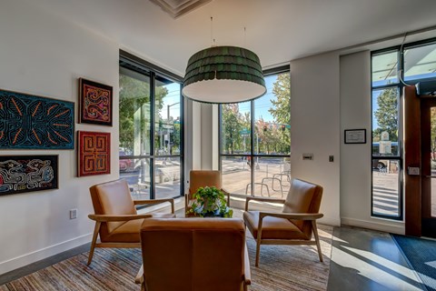 A room with a brown couch, two chairs and a table with a plant on it.