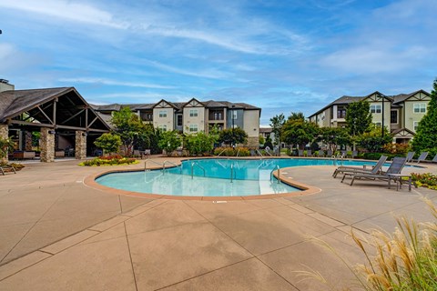 A swimming pool surrounded by lounge chairs and apartment buildings.