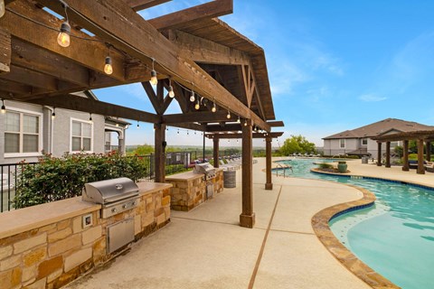 A wooden pergola over a swimming pool with a stone wall and grill.