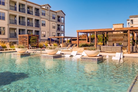 A pool area with lounge chairs and a building in the background.