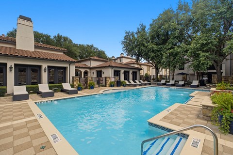 A large swimming pool surrounded by lounge chairs and trees.