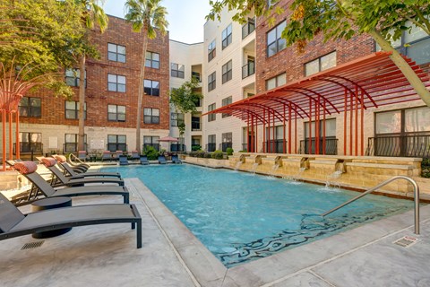 A pool surrounded by lounge chairs and a red awning.