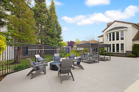 A patio with chairs and a table is surrounded by a fence and trees.