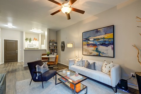A living room with a white couch, a blue chair, and a painting on the wall.