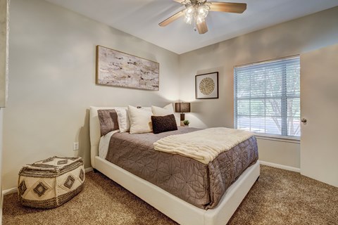 A bedroom with a bed, pillows, a ceiling fan, and a window.