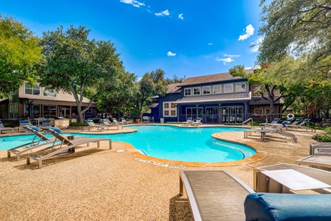 A large outdoor swimming pool surrounded by lounge chairs and trees.