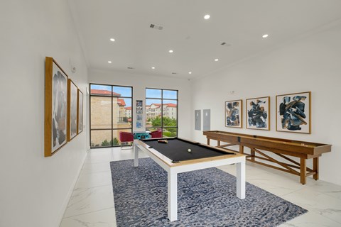 A pool table is in the middle of a room with a blue rug and pictures on the wall.