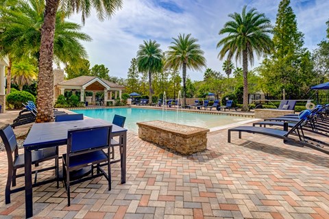 A pool area with a table and chairs and palm trees.